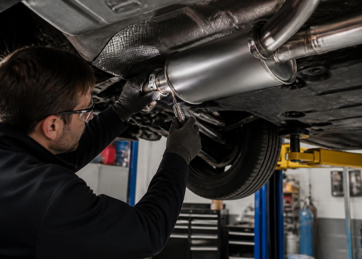 Technician fitting a new muffler and exhaust pipe under a vehicle on a lift